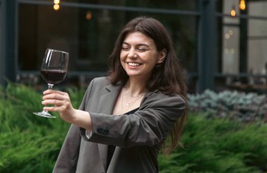 Attractive young woman with glass of red wine outside near restaurant on blurred background, party and celebration concept.