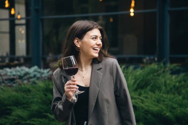 Attractive young woman with glass of red wine outside near restaurant on blurred background, party and celebration concept.