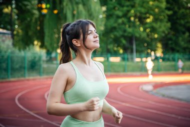 Attractive young woman in sportswear jogging in the stadium in summer.