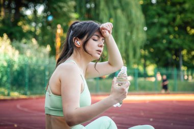 A young woman with a bottle of water in training at the stadium.