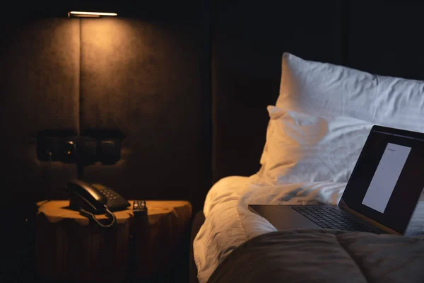 Laptop on the bed at night in the interior of the room by the light of a lamp, copy space.