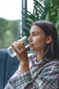 A young woman drinks water in a cafe, the concept of health and maintaining water balance.