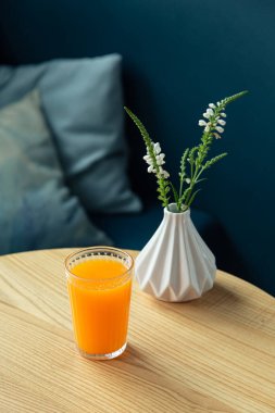 Bir bardak portakal suyu mavi bir vazonun yanındaki masada..