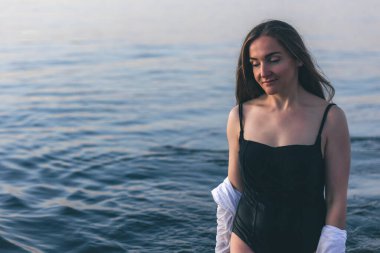 A woman in a bathing suit and a white shirt in the sea at sunset, copy space.