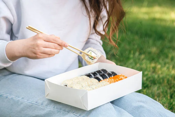 Close up, woman eating sushi in box at picnic, sushi delivery concept.