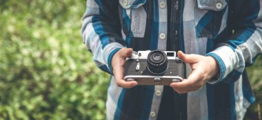 Vintage film camera in the hands of a man on a blurred background, the concept of tourism and camping.
