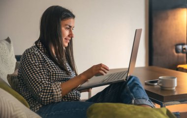 A young woman working on a laptop at home on the couch, the concept of remote work, freelancing.