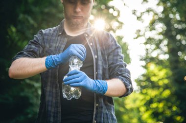 A man in gloves with a plastic bottle in his hands, cleans the forest, the concept of caring for nature and ecology.