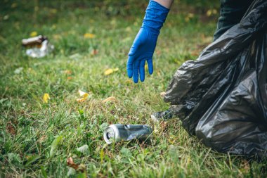 A mans hand in a glove cleans up garbage in the forest, care for the environment and ecology.