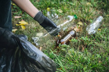 A man puts a plastic bottle in a garbage bag, the concept of forest cleaning and love for nature.