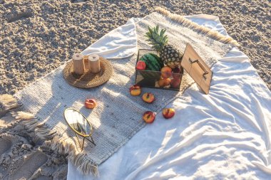 Plaid with fruits on the sandy seashore, summer picnic by the sea at sunset.