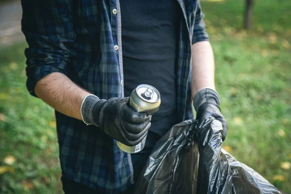 A man with a garbage bag in the forest cleans up bottles, the concept of love for nature and care for the ecology.