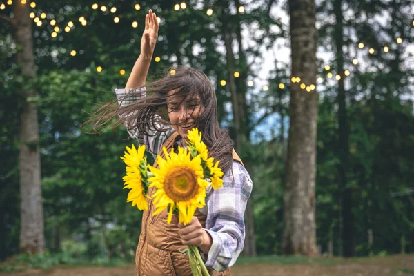 A young woman with a bouquet of sunflowers on a blurred background in nature with bokeh light bulbs.
