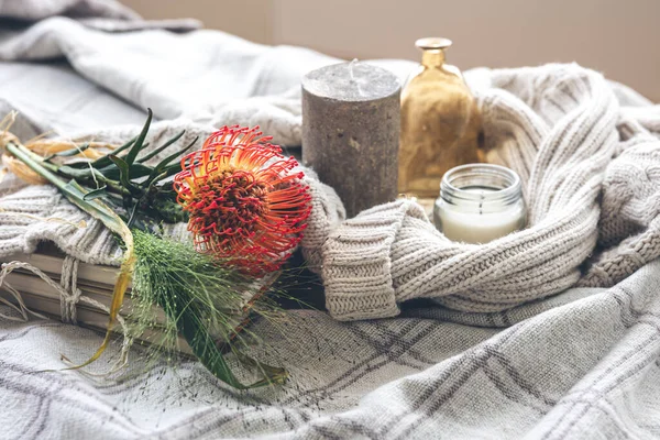 Cozy home composition with a flower, candles and a knitted element in a bed in pastel colors.
