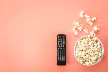 Remote control and plate with popcorn on a pink background, flat lay, minimalism.