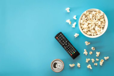 A bowl of popcorn, a can of drink on a blue background, the concept of watching TV, movies, series.