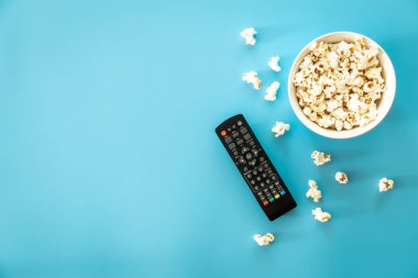 TV remote control and popcorn on a blue background, the concept of watching movies, TV shows, minimalism.