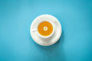 A cup of chamomile tea on a blue background, flat lay, minimalism.
