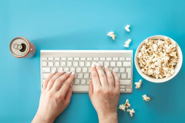 Keyboard, female hands and popcorn on a blue background, the concept of watching movies, series, minimalism.