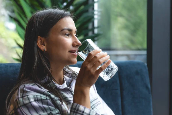 A young woman drinks water in a cafe, the concept of health and maintaining water balance.
