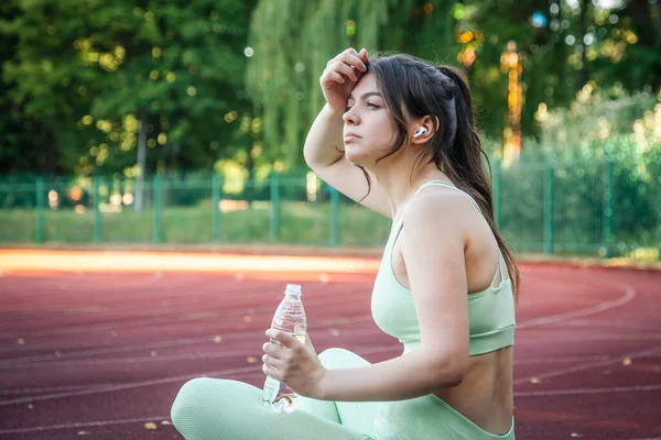 A young woman with a bottle of water in training at the stadium.