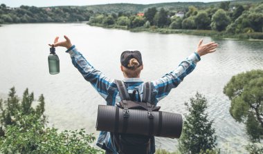 Male traveler with backpack and karimat in nature by the lake, tourism concept.