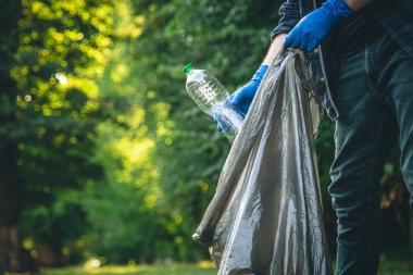 A man puts a plastic bottle in a garbage bag, the concept of forest cleaning and love for nature.