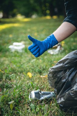 A mans hand in a glove cleans up garbage in the forest, care for the environment and ecology.