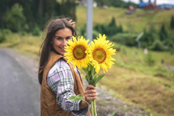 A young woman with a bouquet of sunflowers in nature in the mountains in a rural area.