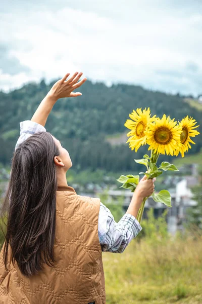 Woman with a bouquet of sunflowers in nature in the mountains, copy space.