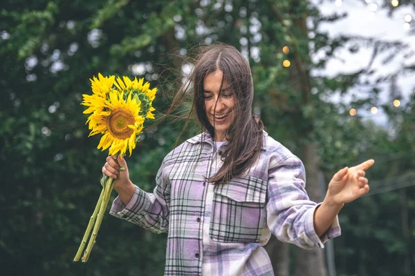 A young woman with a bouquet of sunflowers on a blurred background in nature with bokeh light bulbs.