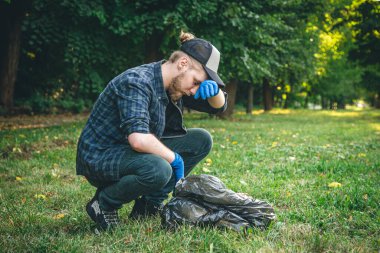 A young man with a garbage bag in the forest cleans up plastic bottles, the concept of love for nature and care for the ecology, copy space.