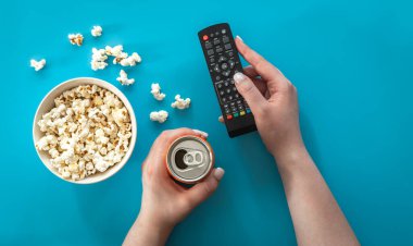 Female hands and popcorn on a blue background, the concept of watching movies, series, minimalism.