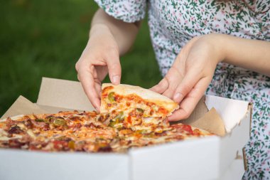 Female hands take a piece of pizza from the box, close-up.