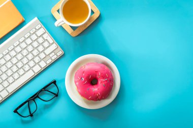 Donut, tea and keyboard on blue background, flat lay, workplace and creativity concept.
