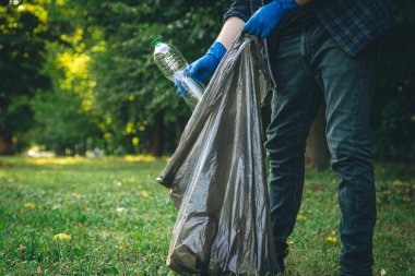 A man puts a plastic bottle in a garbage bag, the concept of forest cleaning and love for nature.