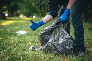 A mans hand in a glove cleans up garbage in the forest, care for the environment and ecology.