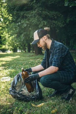 A man puts a plastic bottle in a garbage bag, the concept of forest cleaning and love for nature.