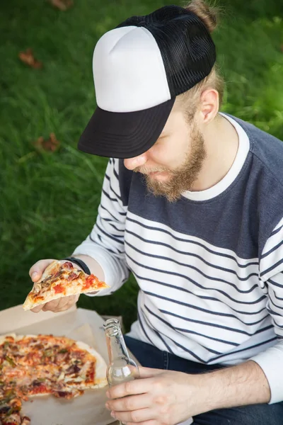 A young man eating pizza on a picnic, close-up.