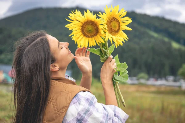 A young woman with a bouquet of sunflowers in nature in the mountains in a rural area.