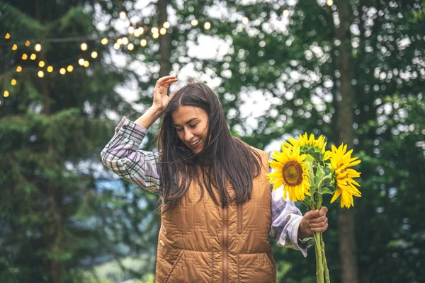 A young woman with a bouquet of sunflowers on a blurred background in nature with bokeh light bulbs.