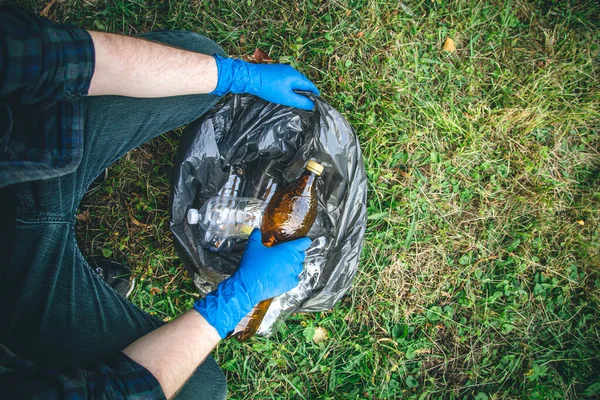 A man puts a plastic bottle in a garbage bag, the concept of forest cleaning and love for nature.