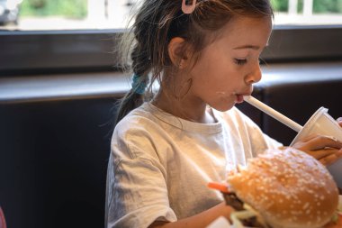 A little girl in a cafe eats fast food, a burger and fries.