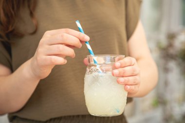 Close-up, a glass of cooling lemonade in female hands.