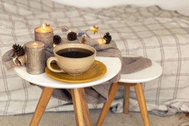 Cozy autumn composition with a cup of tea, candles and decorative details on a blurred background.