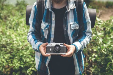 Vintage film camera in the hands of a man on a blurred background, the concept of tourism and camping.