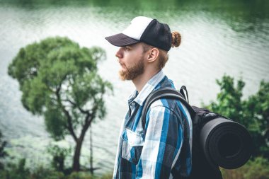Male traveler with backpack and karimat in nature by the lake, tourism concept.