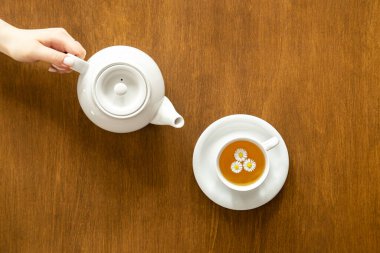 A cup of chamomile tea and a teapot on a wooden background, flat lay, minimalism.