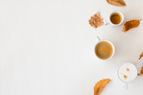 Autumn composition with cups of coffee and leaves on a textural white background, flat lay, copy space.