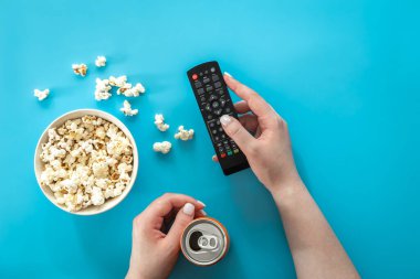 Female hands and popcorn on a blue background, the concept of watching movies, series, minimalism.